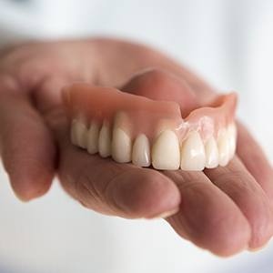 Hand holding a dental restoration | Full and Partial Dentures Andover MA 01810