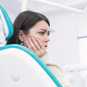 Woman in dental chair holding jaw